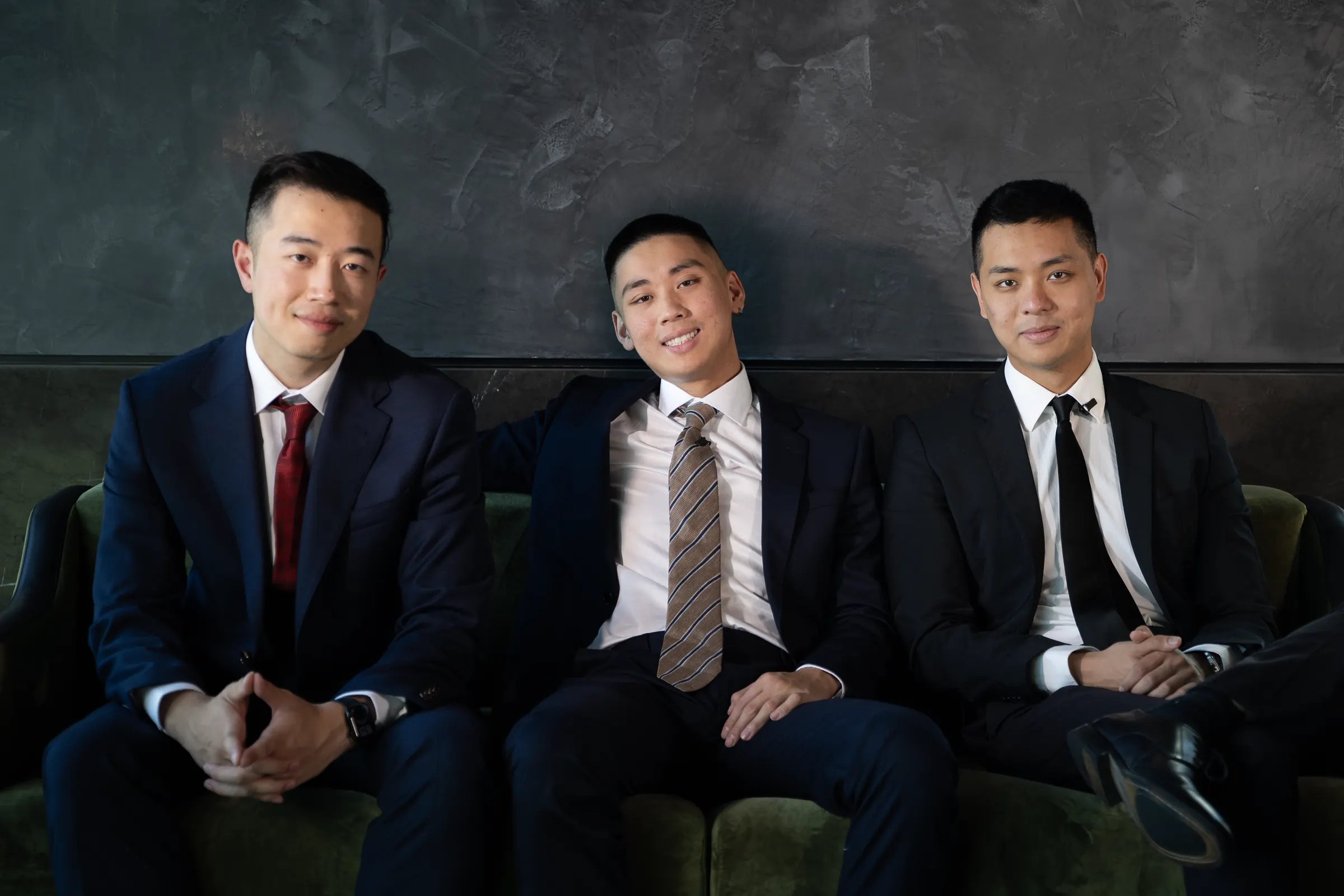 Terence Mok, Jordan Pham and Stanley Ma sitting together on a green velvet sofa against a charcoal wall.