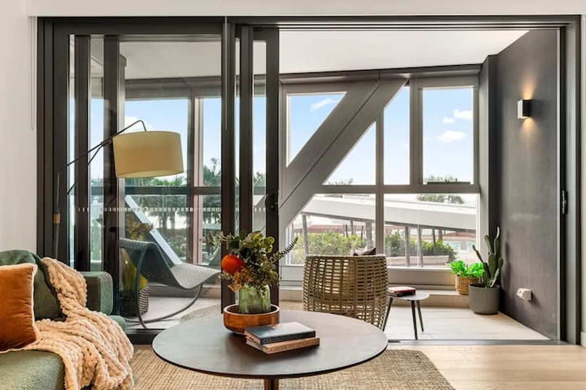 A sunroom with a rattan chair, a floor lamp and a round coffee table with books and flowers.