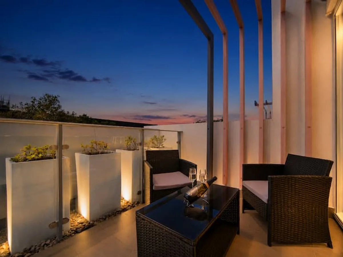 A private terrace at dusk with wicker armchairs, a glass table and lit planter boxes.